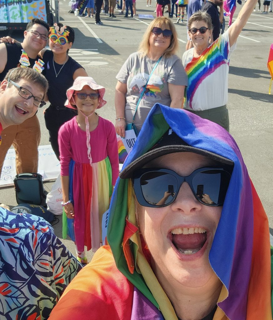 Selfie picture of the FCC attendees at OC Pride 2024. Pastor Monica is front and center wearing a rainbow pride flag on her head.