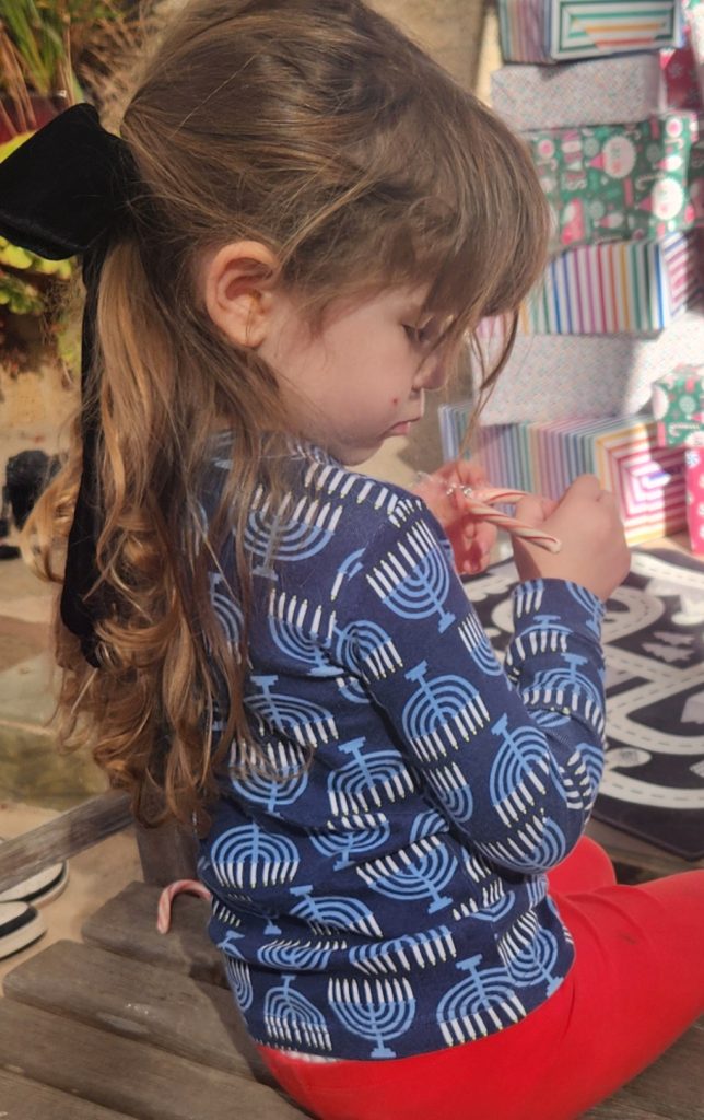 Small child with a candy-cane wearing a Chanukah long sleeve shirt with menoras.