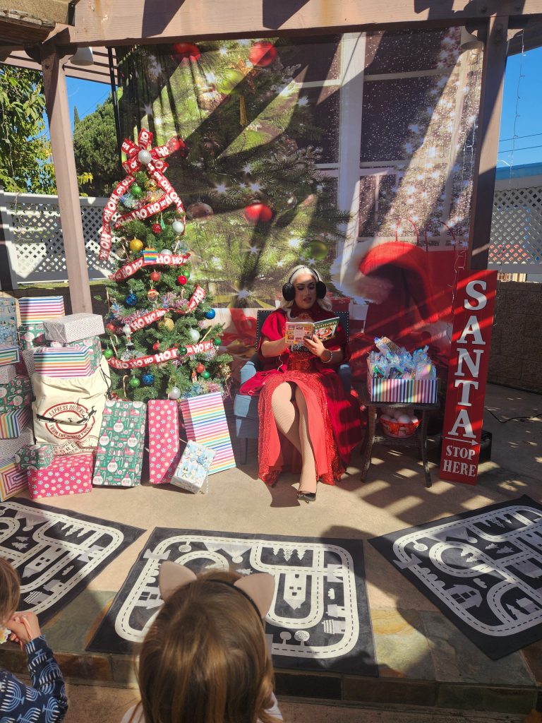 Mrs. Claus reading from santa's seat by the tree to kids directly facing Mrs. Claus