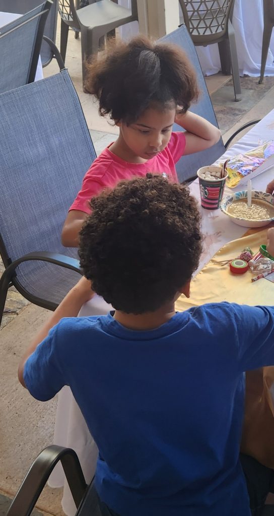 2 kids at a table with food and crafts.