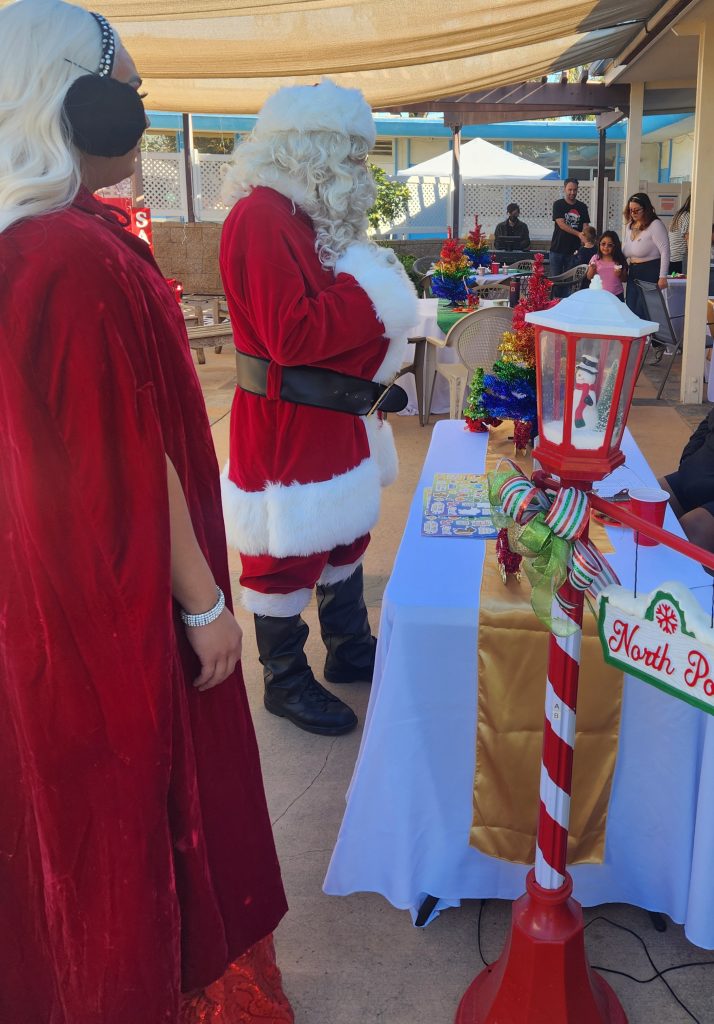 Mr. and Mrs. Claus looking at a display table and into the patio.